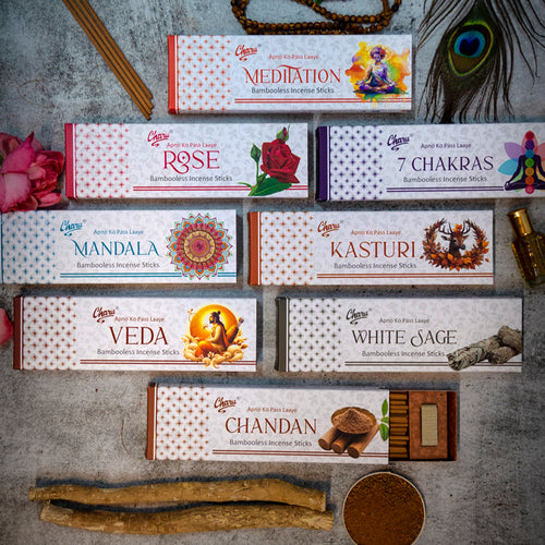 Flat lay display of Charu Perfumery smudge incense sticks in variants like Meditation, Rose, 7 Chakras, White Sage, and Chandan, styled with herbs, flowers, and spiritual elements on a grey background.