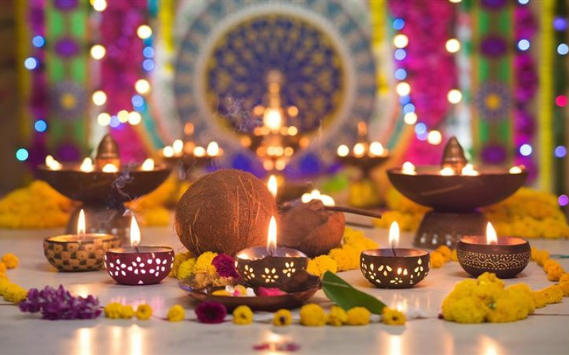 a vibrant image of burning Diyas and some flowers placed on a white marble surface