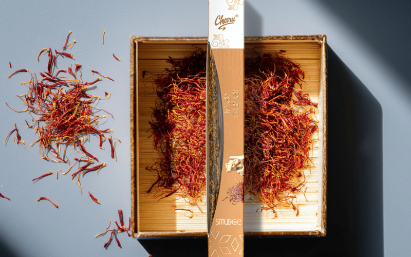 Kesar Chandan agarbatti placed over a bed of saffron strands in a wooden box, with loose saffron and incense powder nearby. 
