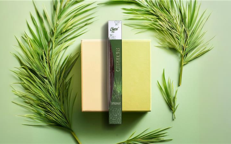 Charu Citronella Smudge Incense Sticks pack surrounded by some lemon grass leaves placed on the green surface